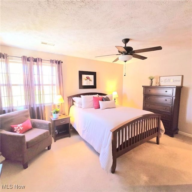 bedroom featuring a textured ceiling, carpet floors, visible vents, and ceiling fan