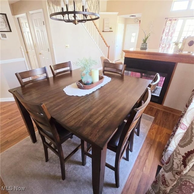 dining room featuring wood finished floors, a notable chandelier, baseboards, and stairway