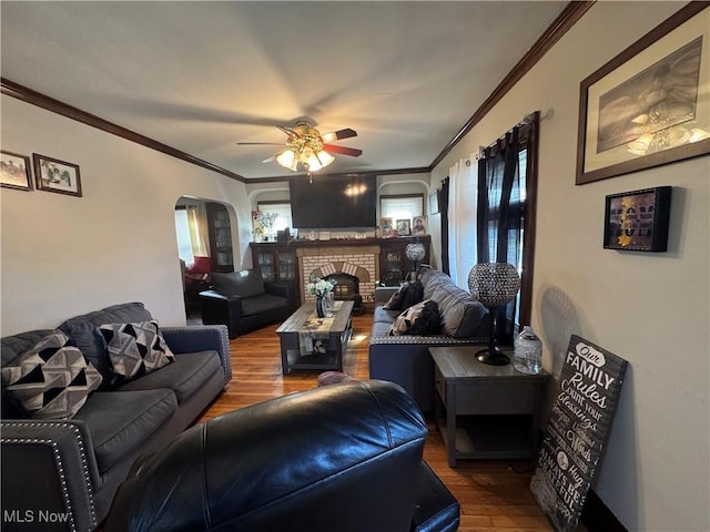 living area featuring arched walkways, wood finished floors, ornamental molding, and ceiling fan