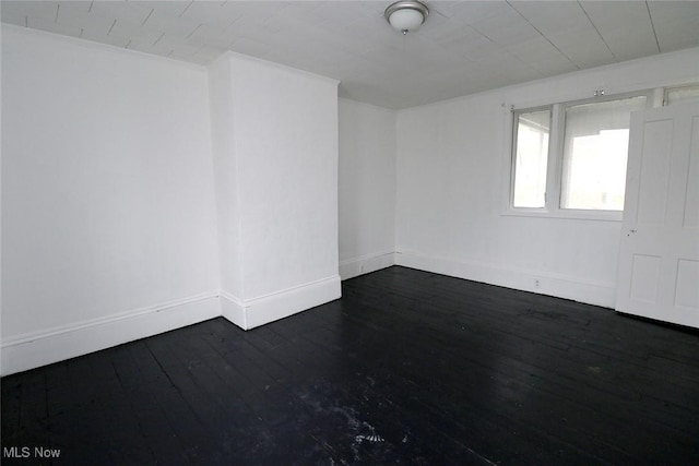 unfurnished room featuring baseboards and dark wood-style flooring