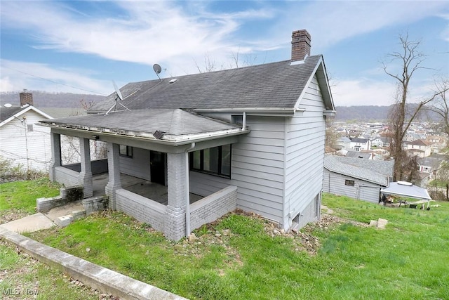 back of house featuring a chimney, a yard, and a shingled roof