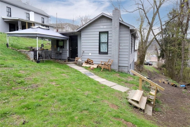 rear view of property with a chimney, a gazebo, and a yard