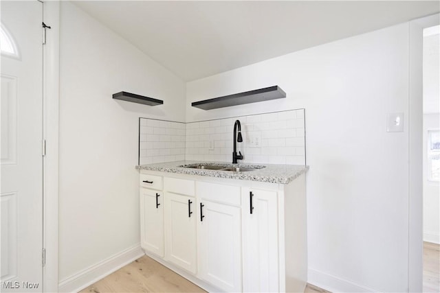 kitchen with lofted ceiling, light stone counters, backsplash, a sink, and light wood-type flooring