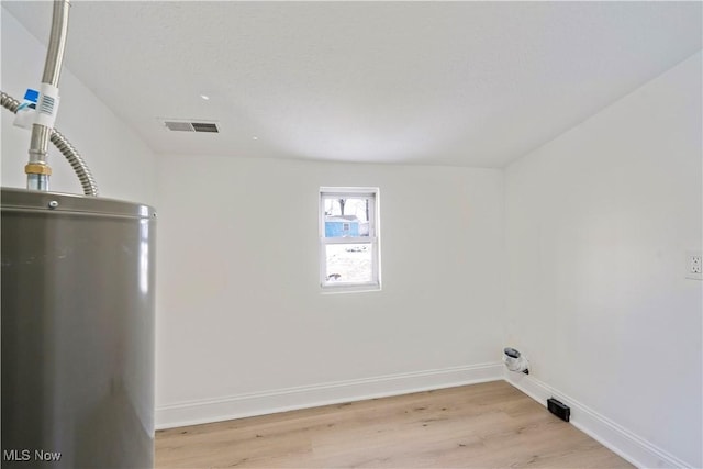 laundry area with baseboards, water heater, visible vents, and light wood-style flooring