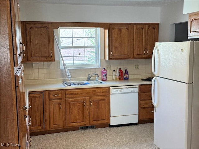 kitchen with a sink, tasteful backsplash, visible vents, white appliances, and brown cabinetry