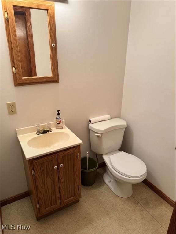 half bathroom featuring baseboards, toilet, and vanity