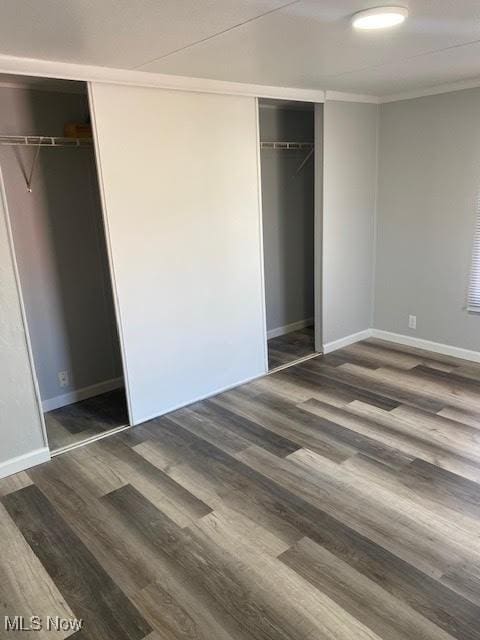 unfurnished bedroom with wood finished floors, a closet, crown molding, and baseboards