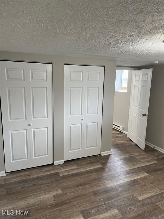 unfurnished bedroom with two closets, a baseboard radiator, and a textured ceiling
