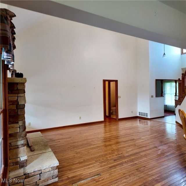 unfurnished living room with a towering ceiling, baseboards, visible vents, stairs, and wood-type flooring