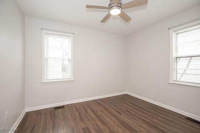 empty room featuring visible vents, dark wood finished floors, and a healthy amount of sunlight