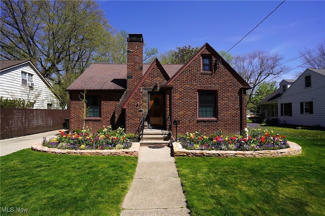 tudor house with brick siding, fence, a chimney, and a front yard