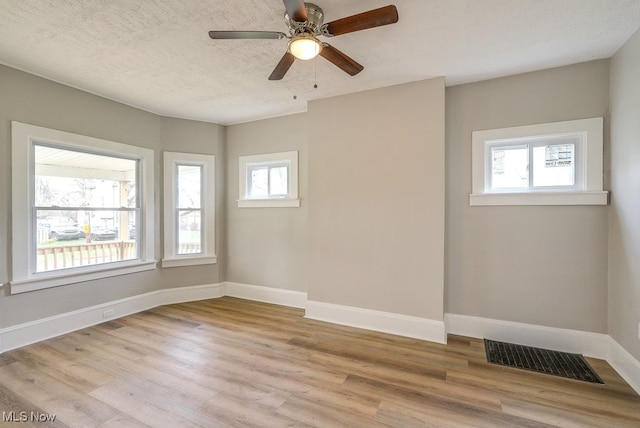 unfurnished room with a wealth of natural light, visible vents, light wood finished floors, and baseboards