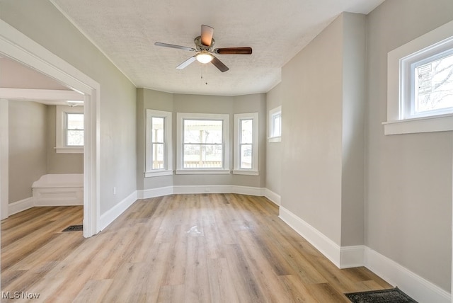 empty room featuring light wood-style floors, a wealth of natural light, a ceiling fan, and a textured ceiling