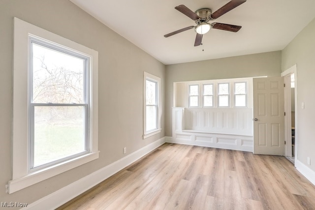 empty room featuring plenty of natural light, baseboards, light wood-style floors, and ceiling fan