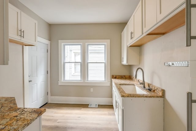kitchen with light stone countertops, light wood-style flooring, visible vents, and a sink