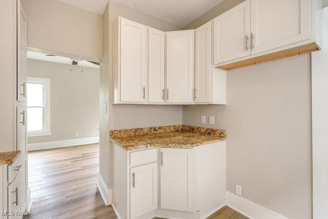 kitchen featuring baseboards, white cabinetry, light stone countertops, and light wood finished floors
