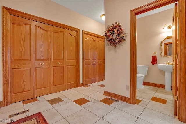 corridor featuring baseboards, visible vents, a sink, and light tile patterned flooring