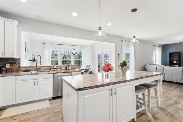 kitchen featuring a breakfast bar, light wood-style flooring, stainless steel dishwasher, and a sink
