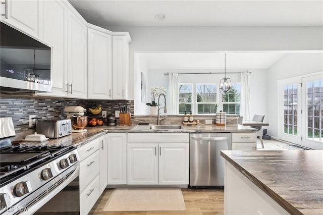 kitchen featuring white cabinets, a sink, tasteful backsplash, light wood-type flooring, and appliances with stainless steel finishes