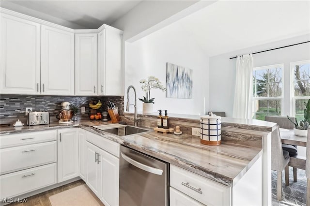 kitchen featuring a peninsula, stainless steel dishwasher, a sink, backsplash, and lofted ceiling