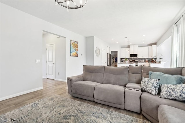 living area featuring recessed lighting, baseboards, an inviting chandelier, and light wood-type flooring