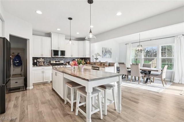 kitchen featuring a kitchen breakfast bar, light wood-style flooring, tasteful backsplash, white cabinetry, and appliances with stainless steel finishes