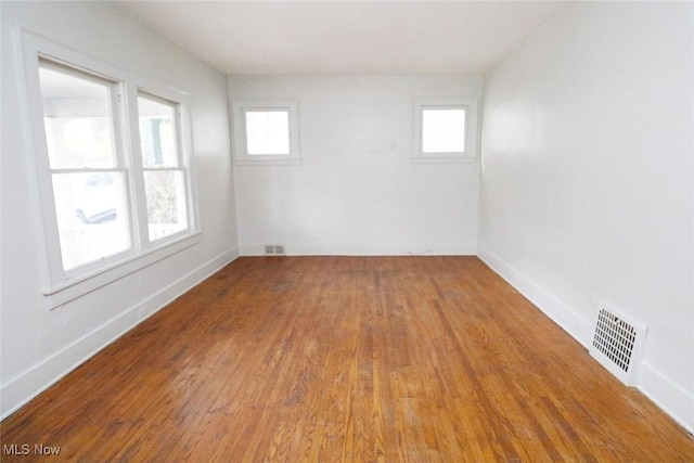 empty room featuring a wealth of natural light, wood finished floors, and visible vents