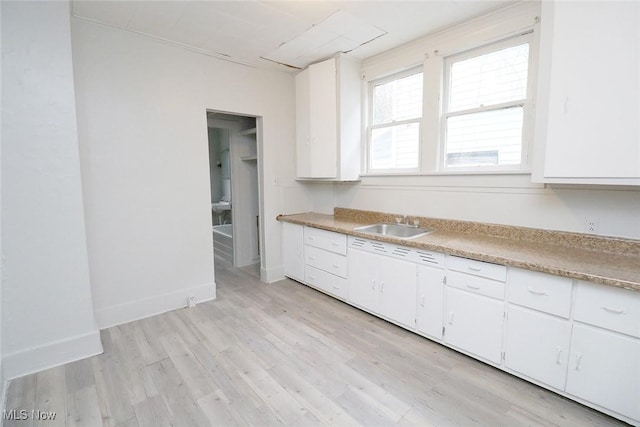 kitchen featuring light countertops, light wood-style floors, white cabinetry, and a sink