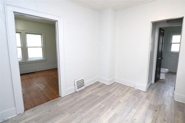 spare room featuring visible vents, a healthy amount of sunlight, light wood-style floors, crown molding, and baseboards