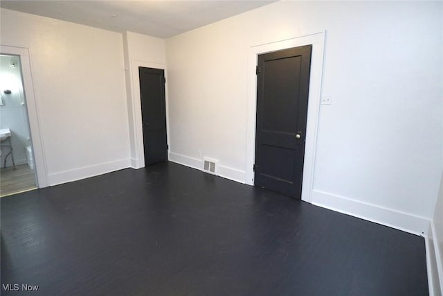 empty room featuring baseboards, dark wood-type flooring, and visible vents