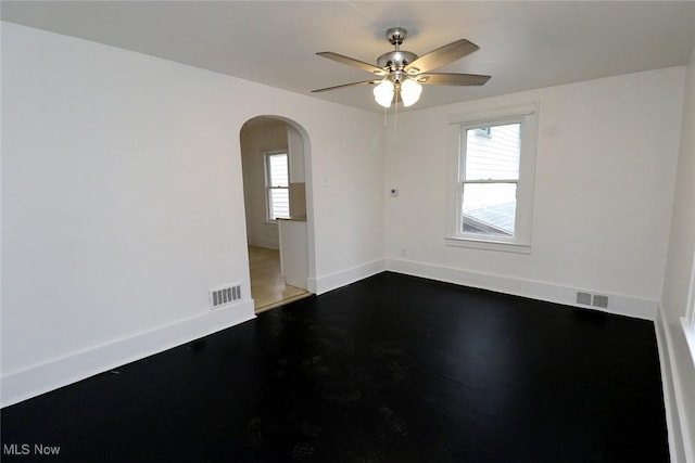 spare room featuring arched walkways, a ceiling fan, visible vents, and baseboards