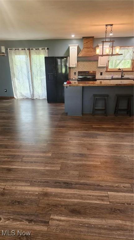 kitchen with white cabinets, premium range hood, dark wood finished floors, black fridge, and stove