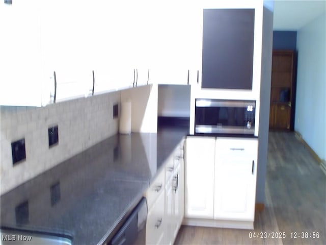 kitchen with stainless steel microwave, tasteful backsplash, white cabinetry, black dishwasher, and wood finished floors