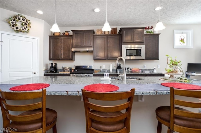 kitchen with stainless steel appliances, a textured ceiling, a sink, dark brown cabinets, and under cabinet range hood