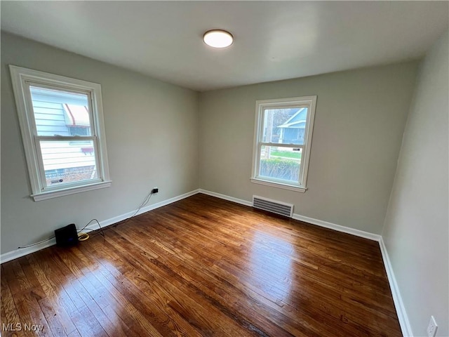 spare room featuring baseboards, visible vents, a wealth of natural light, and dark wood finished floors