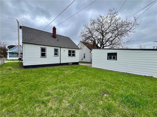back of house featuring a chimney, roof with shingles, and a yard
