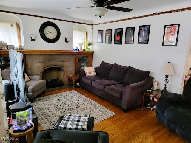 living room featuring ceiling fan, arched walkways, wood finished floors, and a fireplace