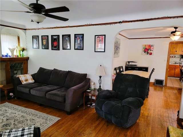 living room with hardwood / wood-style flooring, visible vents, arched walkways, and ceiling fan