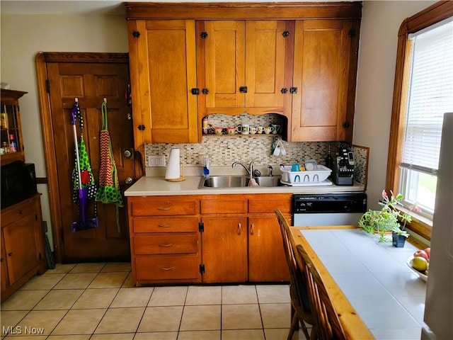kitchen with a sink, tasteful backsplash, black microwave, brown cabinetry, and dishwasher