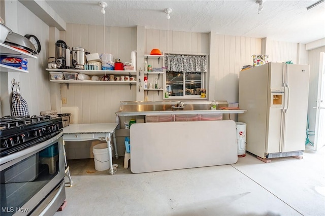 kitchen with white fridge with ice dispenser, concrete floors, stainless steel counters, and stainless steel range with gas stovetop