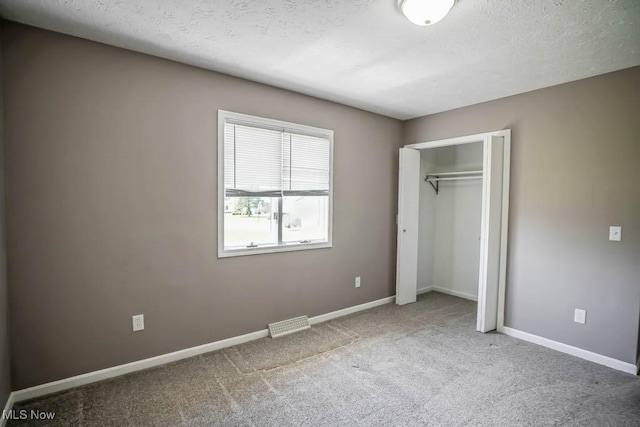 unfurnished bedroom featuring a closet, a textured ceiling, carpet flooring, and baseboards