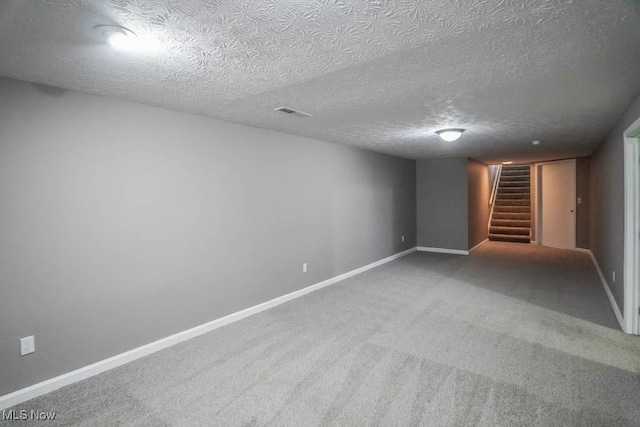 finished below grade area featuring stairway, baseboards, a textured ceiling, and carpet