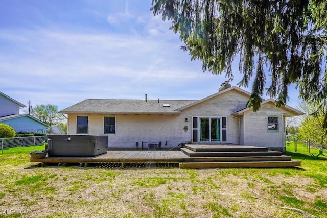 back of property with fence, brick siding, a hot tub, and a deck