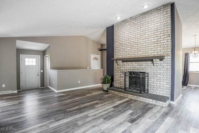 unfurnished living room with wood finished floors, a textured ceiling, a fireplace, baseboards, and lofted ceiling