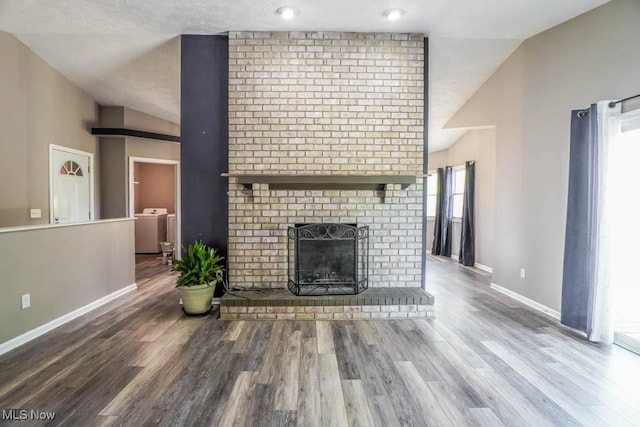 unfurnished living room with lofted ceiling, wood finished floors, baseboards, a fireplace, and washer / clothes dryer