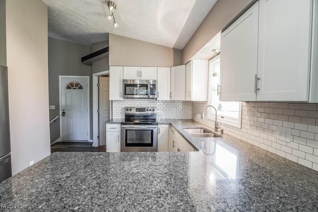 kitchen featuring dark stone countertops, a sink, decorative backsplash, stainless steel appliances, and white cabinets