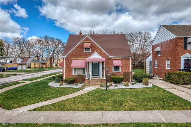 view of front of home featuring a chimney, brick siding, and a front yard