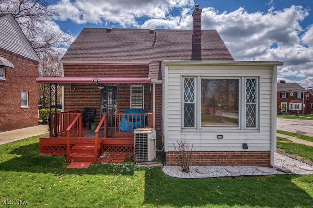 rear view of property featuring central air condition unit, a chimney, a lawn, a shingled roof, and a deck