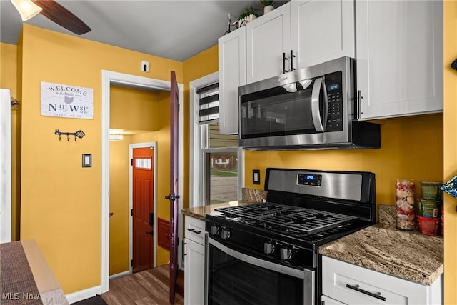 kitchen with stainless steel appliances, dark stone countertops, a ceiling fan, dark wood-type flooring, and white cabinetry