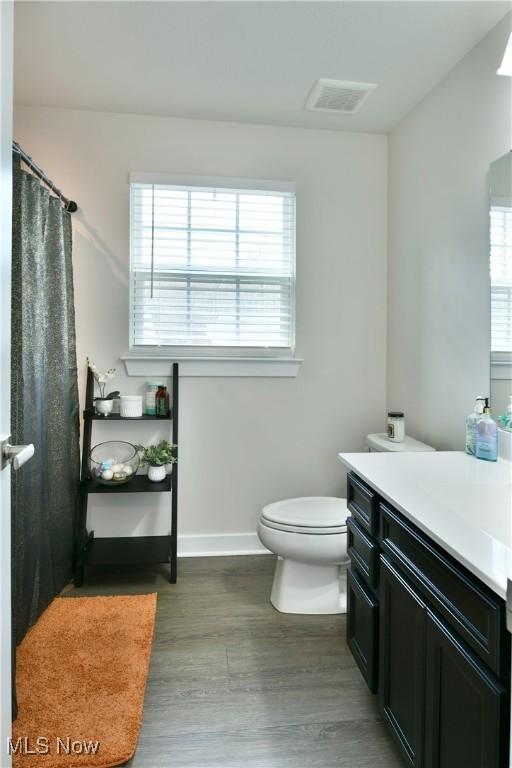 full bathroom with wood finished floors, visible vents, toilet, vanity, and baseboards